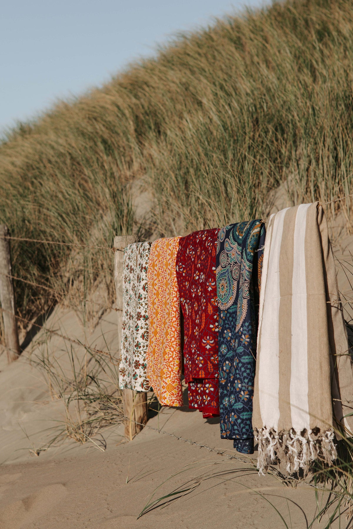 Kleurrijke XXL strandlakens over een houten hek in de duinen