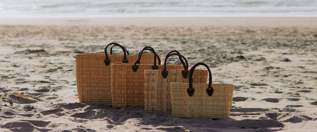 Handgemaakte rieten tassen van Bohemida op een rij op het strand