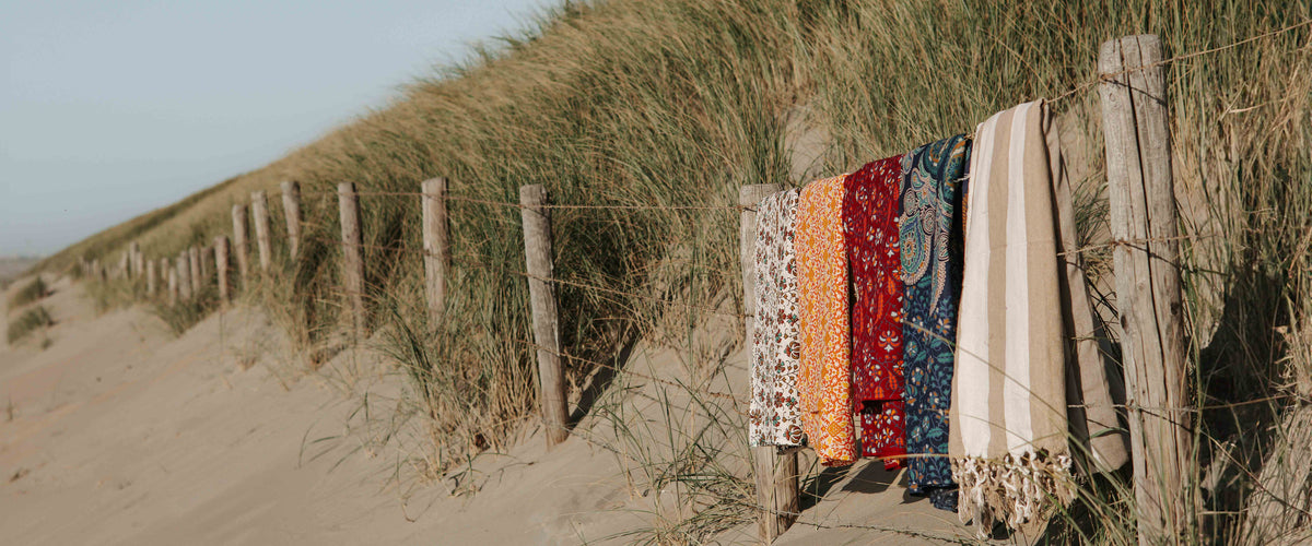 Kleurrijke XXL strandlakens van Bohemida over een hek in de duinen