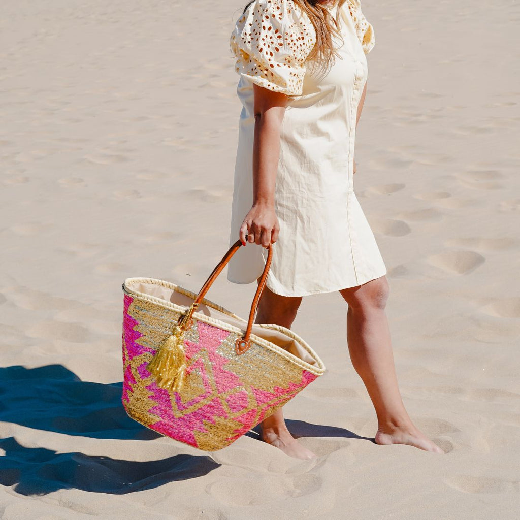 Boho rieten strandtas Aztec goud en fuchsia met gouden tassel, gedragen op het strand