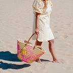 Boho rieten strandtas Aztec goud en fuchsia met gouden tassel, gedragen op het strand