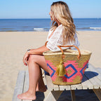 Boho rieten strandtas Aztec goud multi met gouden tassel, naast een vrouw op een bank aan zee