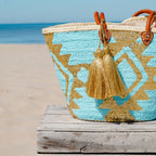 Boho rieten strandtas Aztec goud en turquoise met gouden tassel op een houten bank aan zee