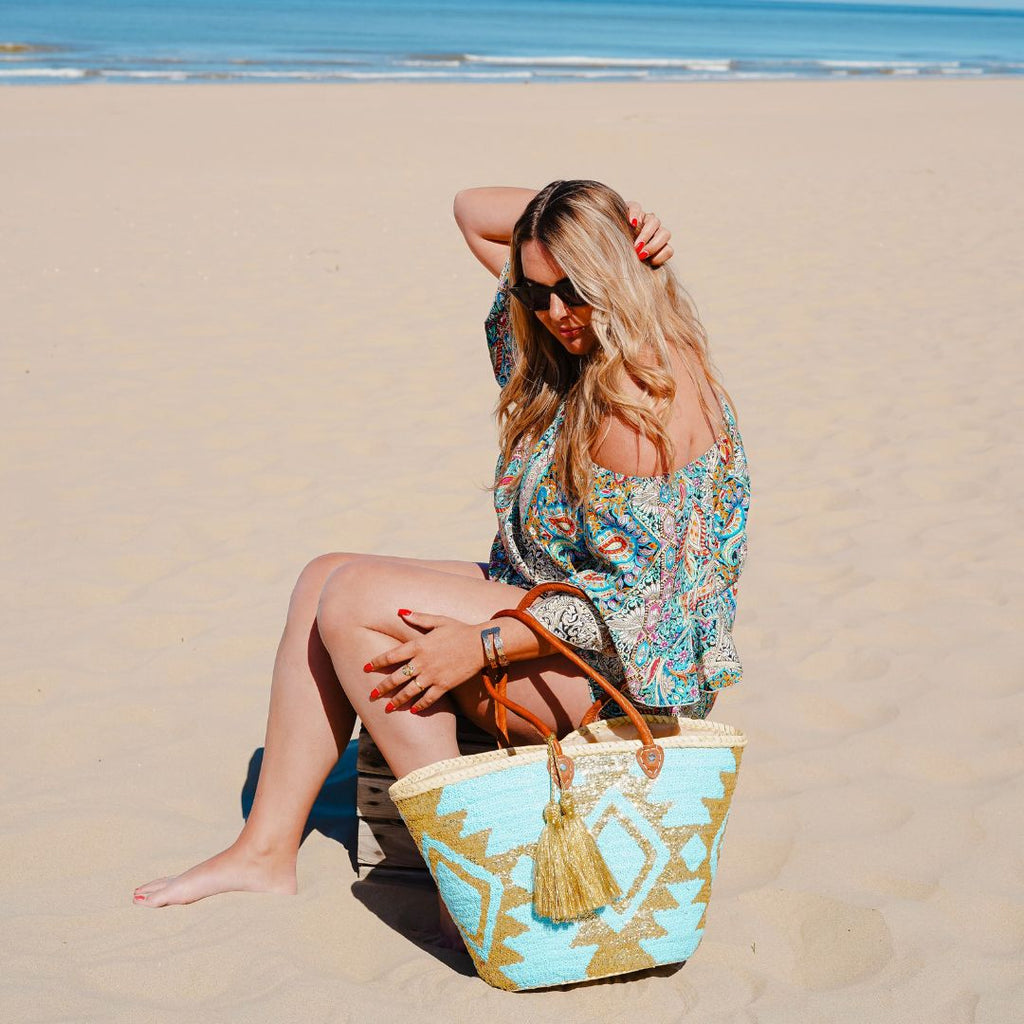 Boho rieten strandtas Aztec goud en turquoise naast een vrouw op het strand