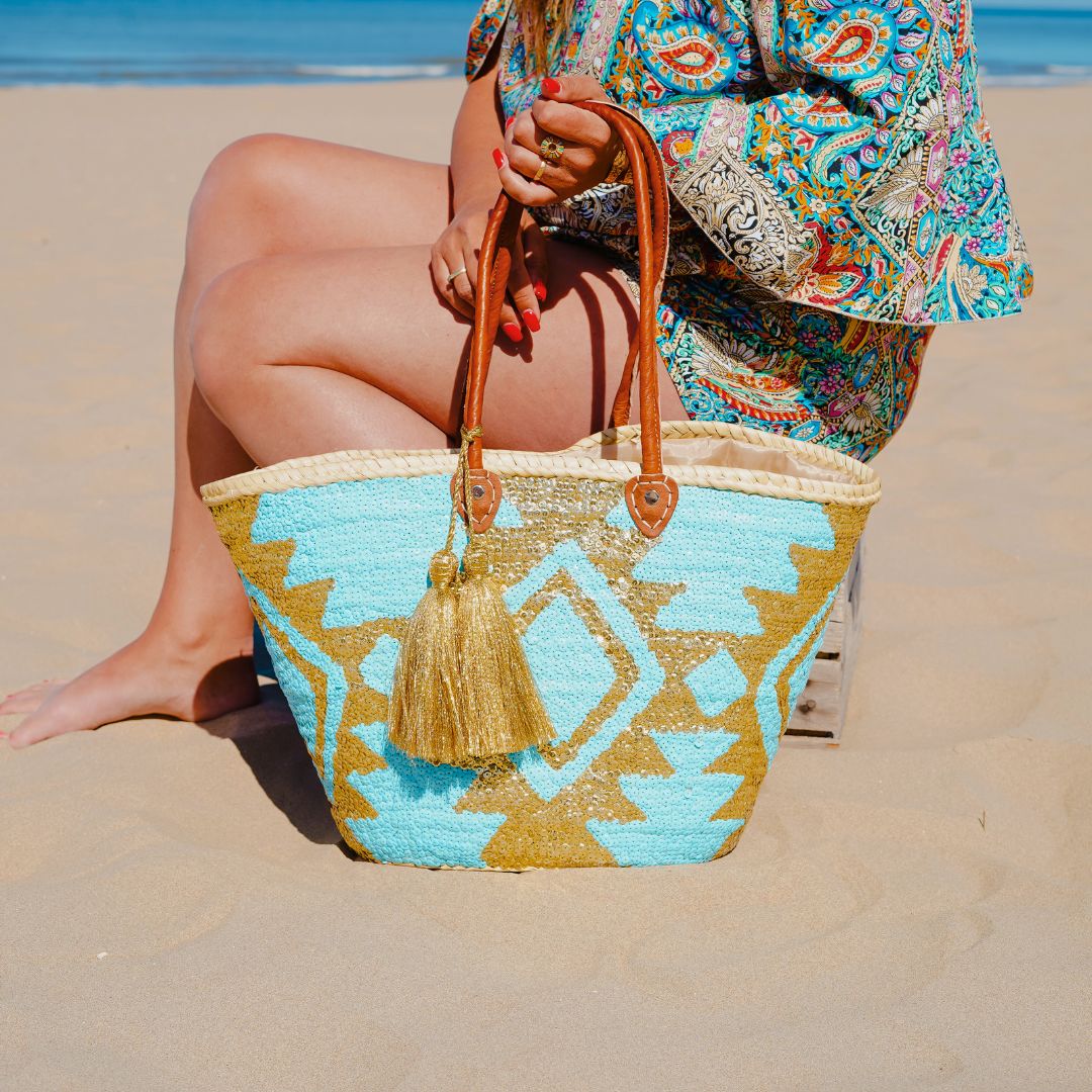 Boho rieten strandtas Aztec goud en turquoise in het zand naast een vrouw
