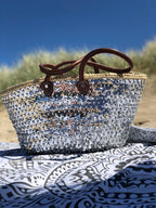 Large straw beach bag with sequins silver, on a beach blanket under a blue sky