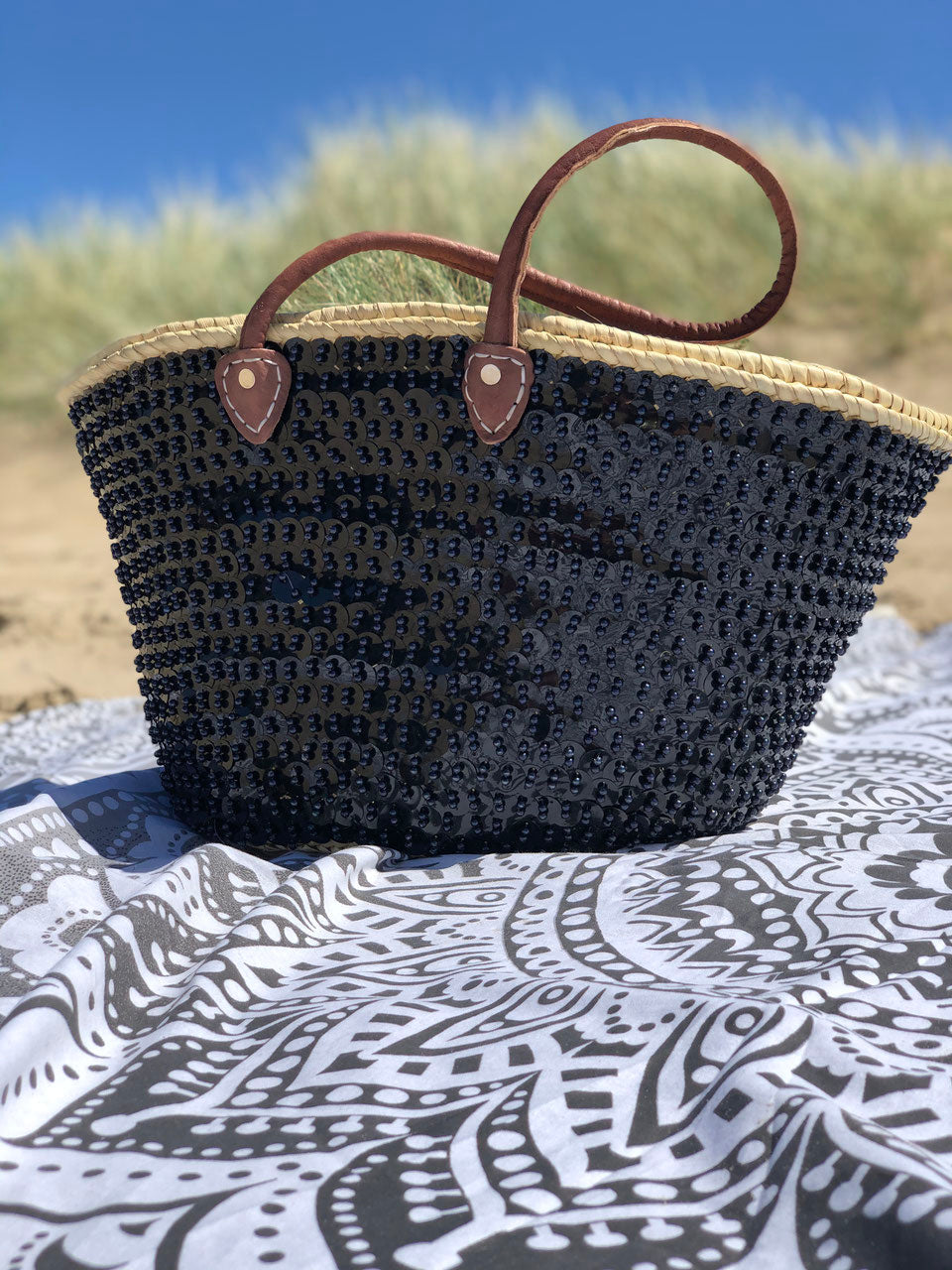 Grote rieten strandtas met pailletten zwart, op een strandlaken in de duinen