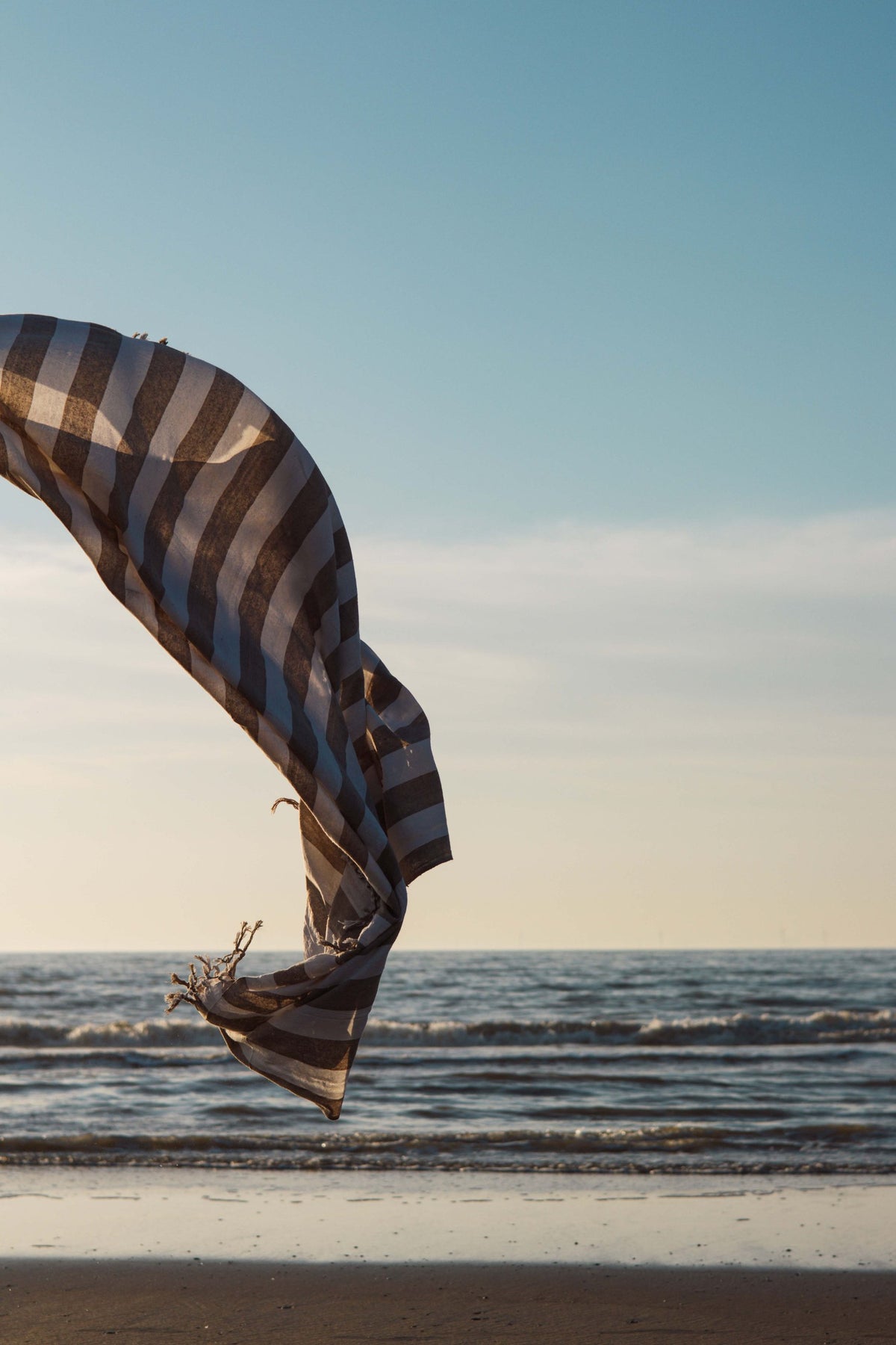 Luxe XXL hamamdoek beige gestreept wapperend in de wind boven zee