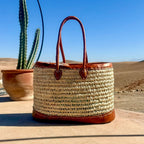 Rieten handtas met leren draaghengsels, naast een cactus in de zon