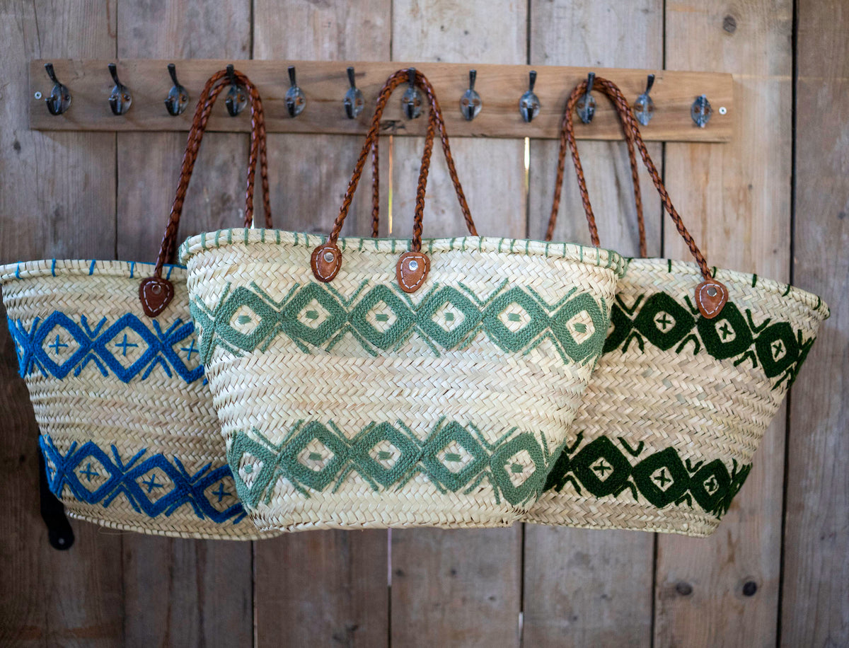 Rieten shopper met kleurrijk borduurwerk donkergroen, met andere kleuren aan een houten wand
