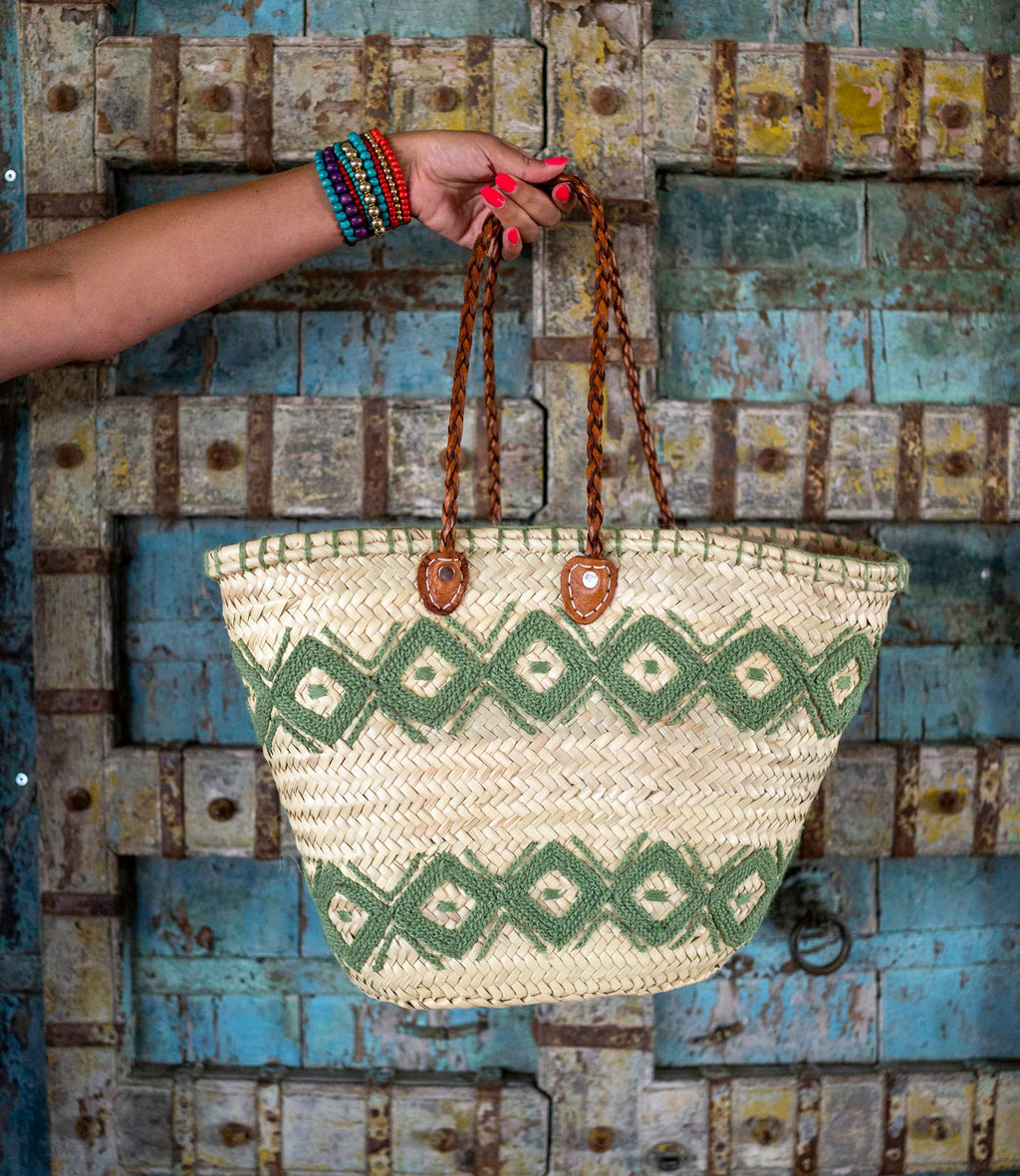 Rattan shopper with colourful embroidery light green, hanging on a wooden wall