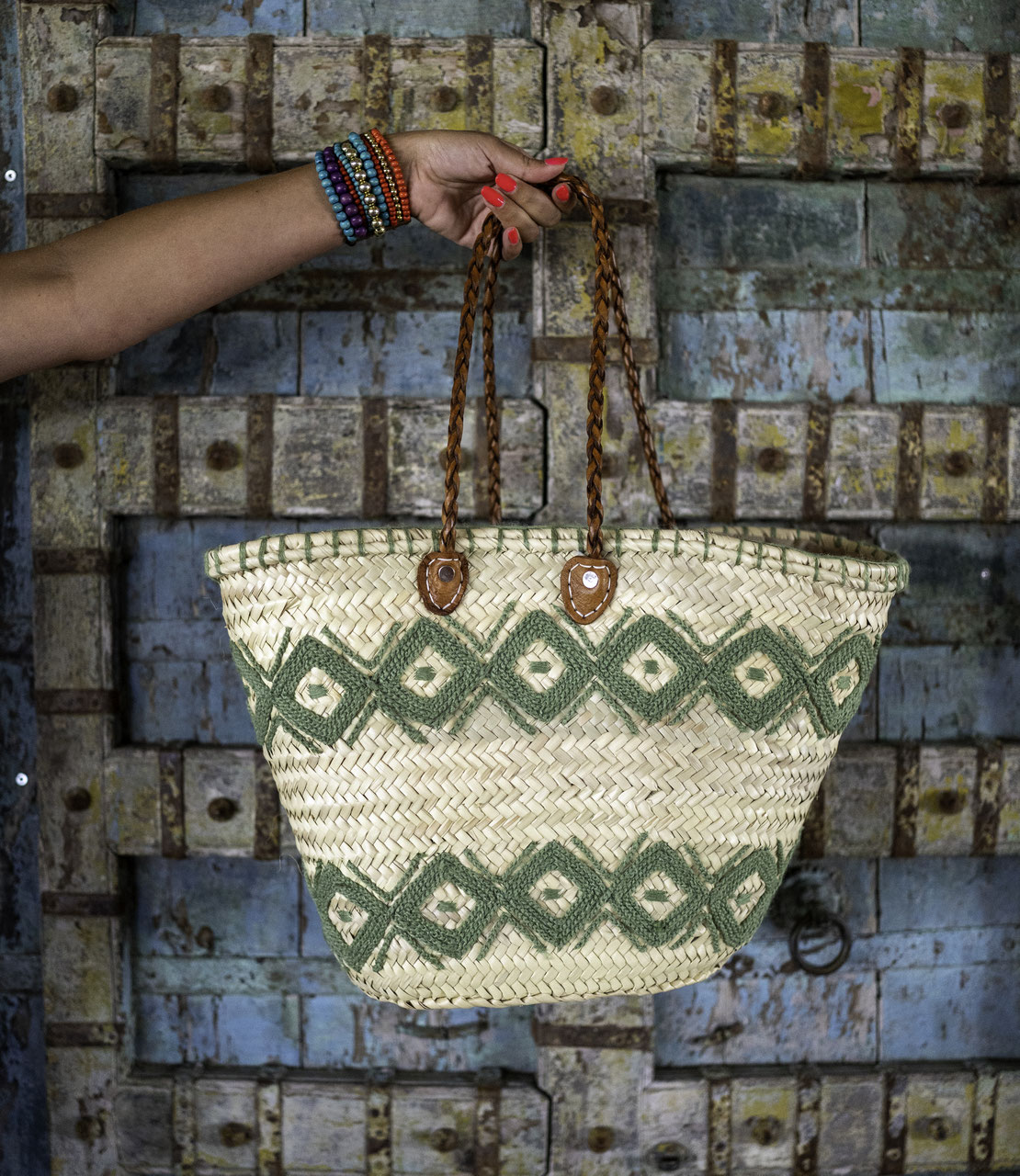 Rattan shopper with colourful embroidery light green, hanging on a wooden wall