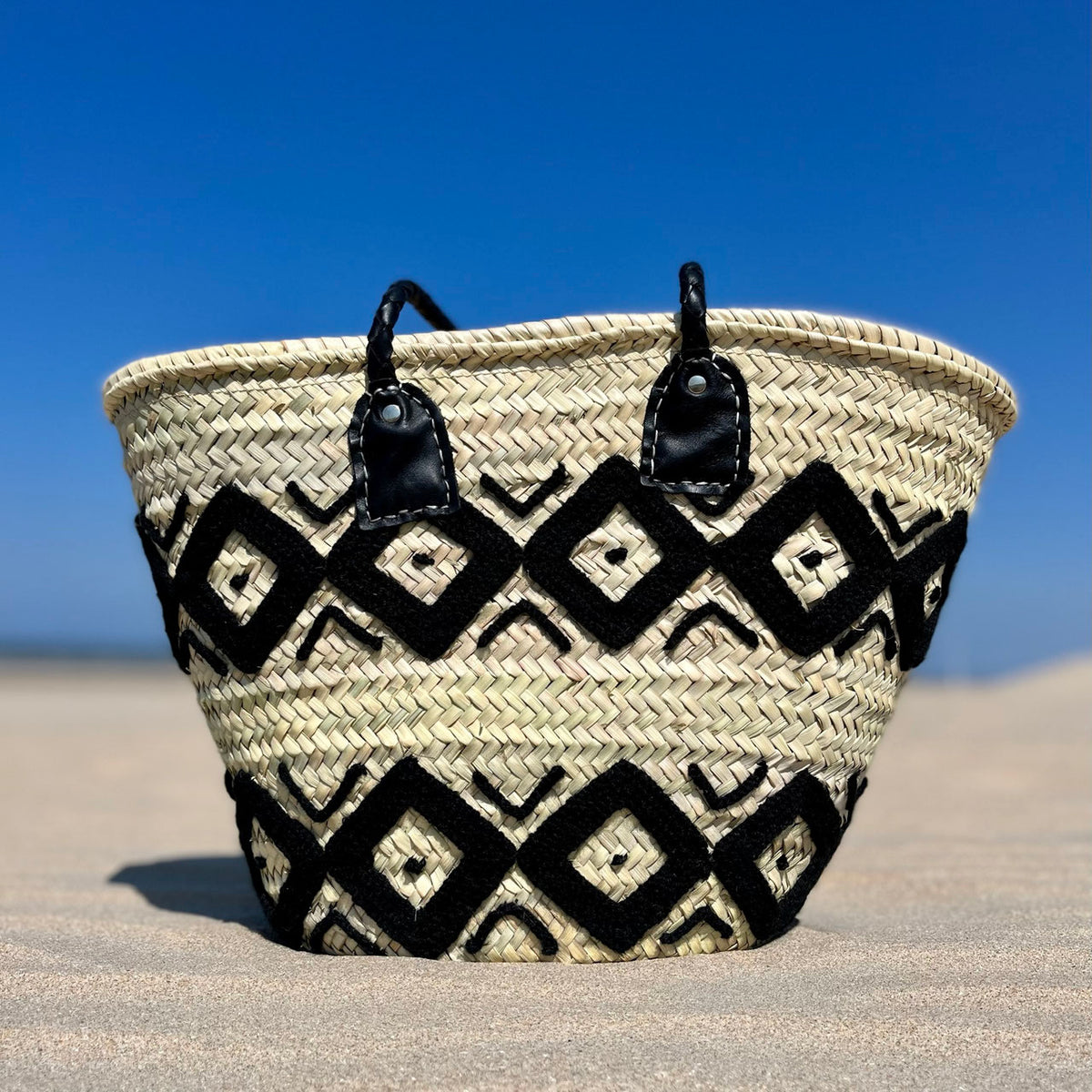 Rieten shopper met kleurrijk borduurwerk zwart, op het strand onder een blauwe lucht