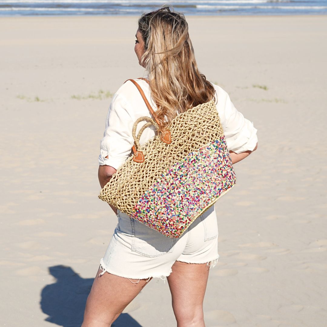 Rieten strandtas Dounia Multi met pailletten, over de schouder gedragen op het strand
