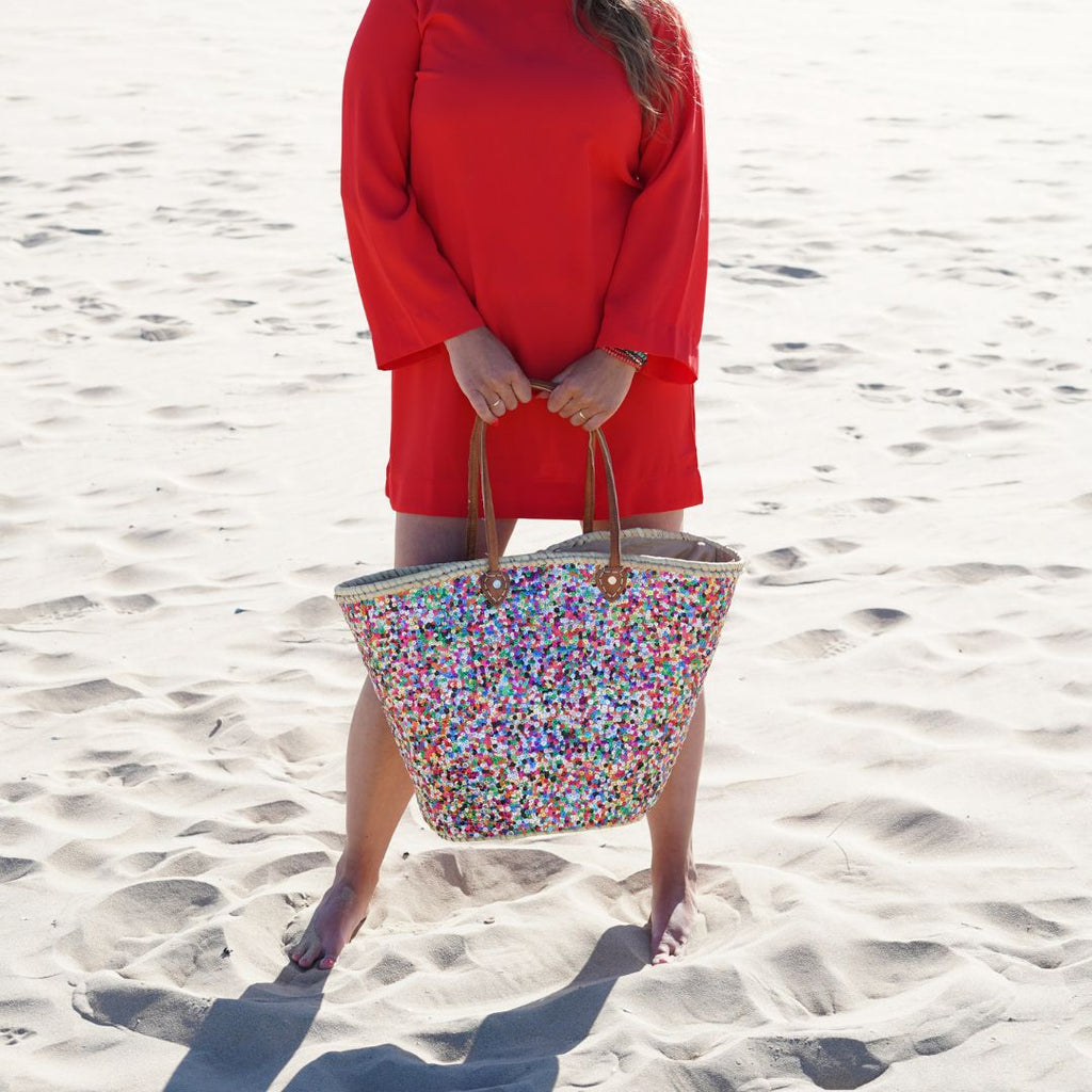 Straw beach bag Multi with colourful sequins, held on the beach