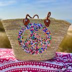 Straw beach bag with sequins Peace multi, on a colourful beach blanket