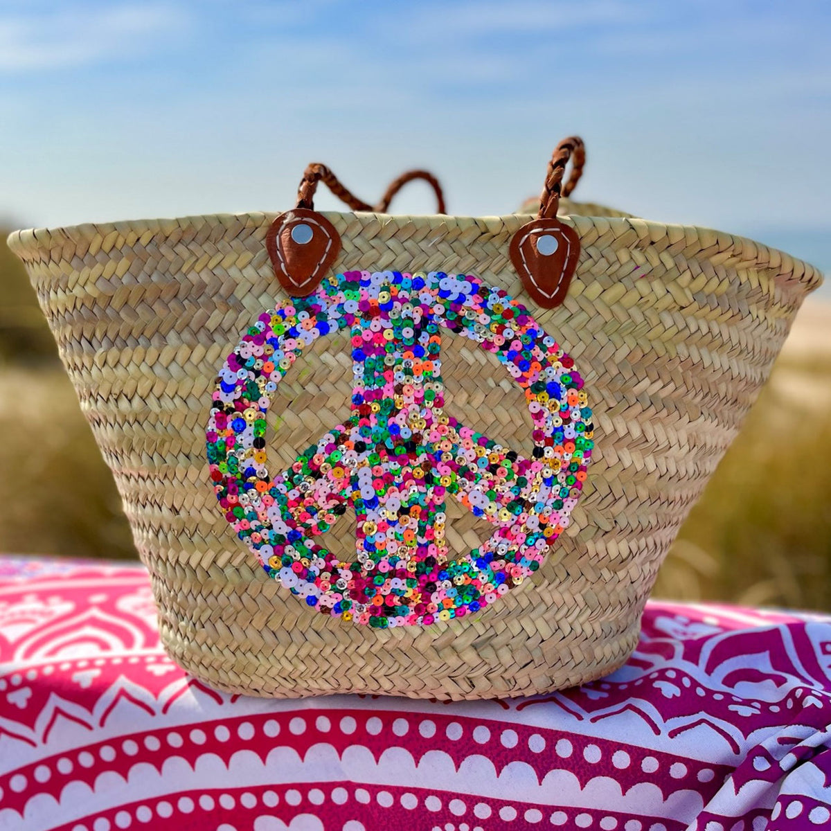 Rieten strandtas met pailletten Peace multi, op een kleurrijk strandlaken