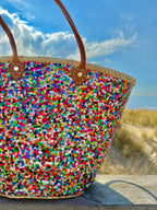 Straw beach bag with sequins pink, purple and green, in the dunes