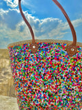 Straw beach bag with sequins pink, purple and green, front view in the dunes