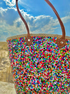 Straw beach bag with sequins pink, purple and green, front view in the dunes