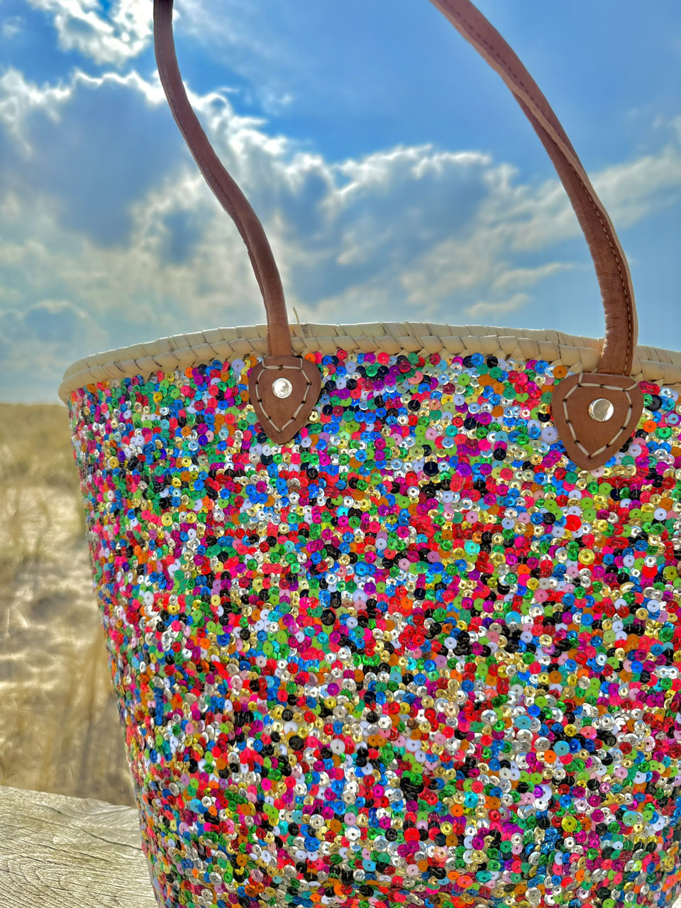 Straw beach bag with sequins pink, purple and green, front view in the dunes