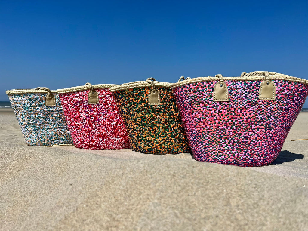 Straw beach bag with sequins pink, red and white, together with other sequin bags on the beach