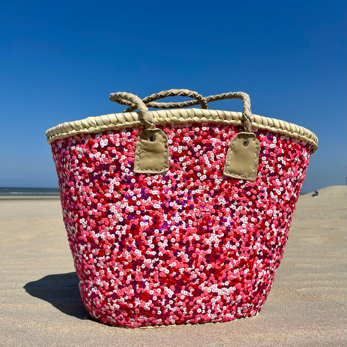 Straw beach bag with sequins pink, red and white, on the beach