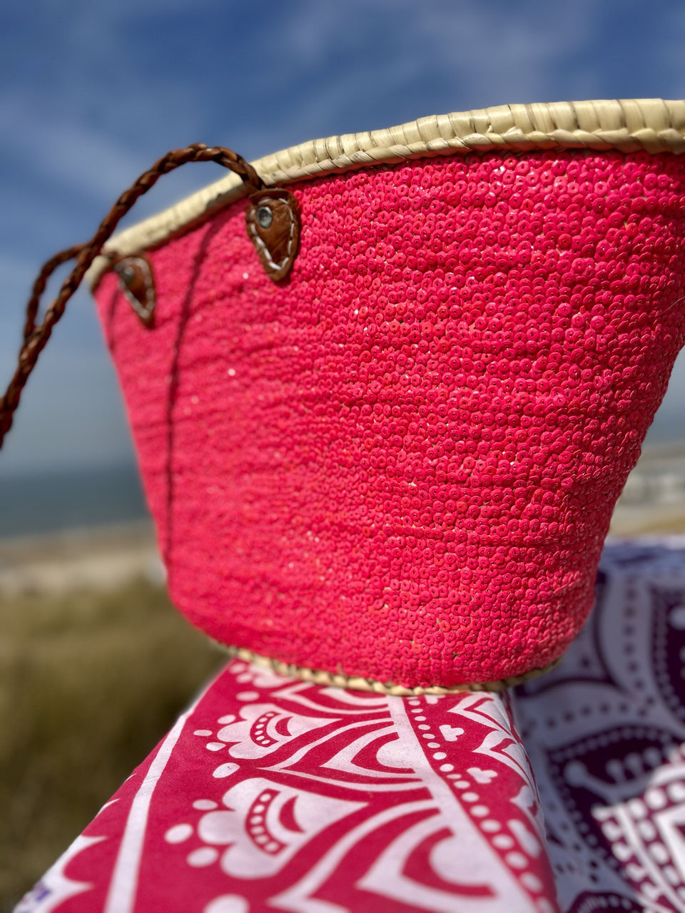 Rieten strandtas met pailletten roze, op een strandlaken
