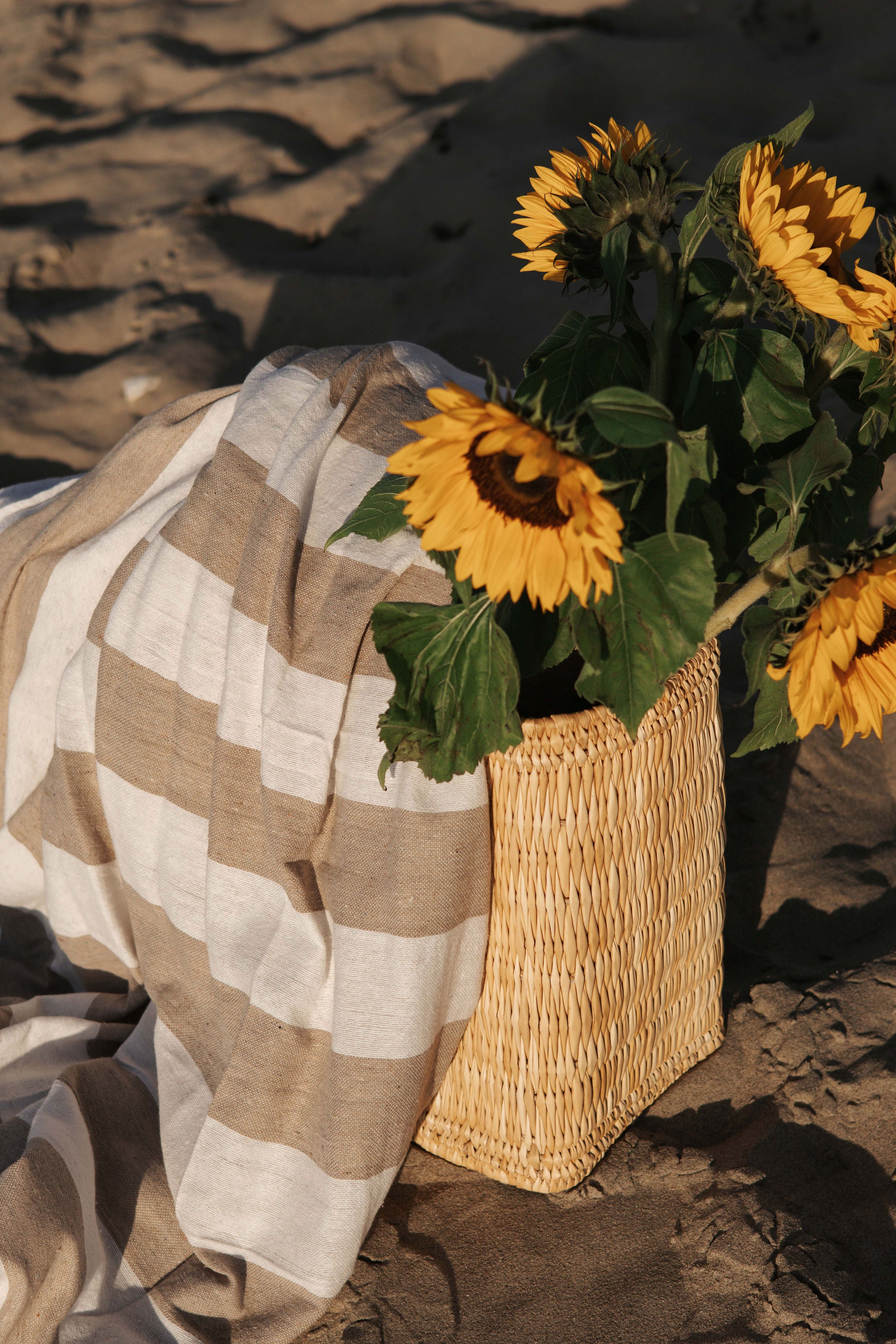 Zonnebloemen in een rieten tas met een gestreept strandlaken op het zand