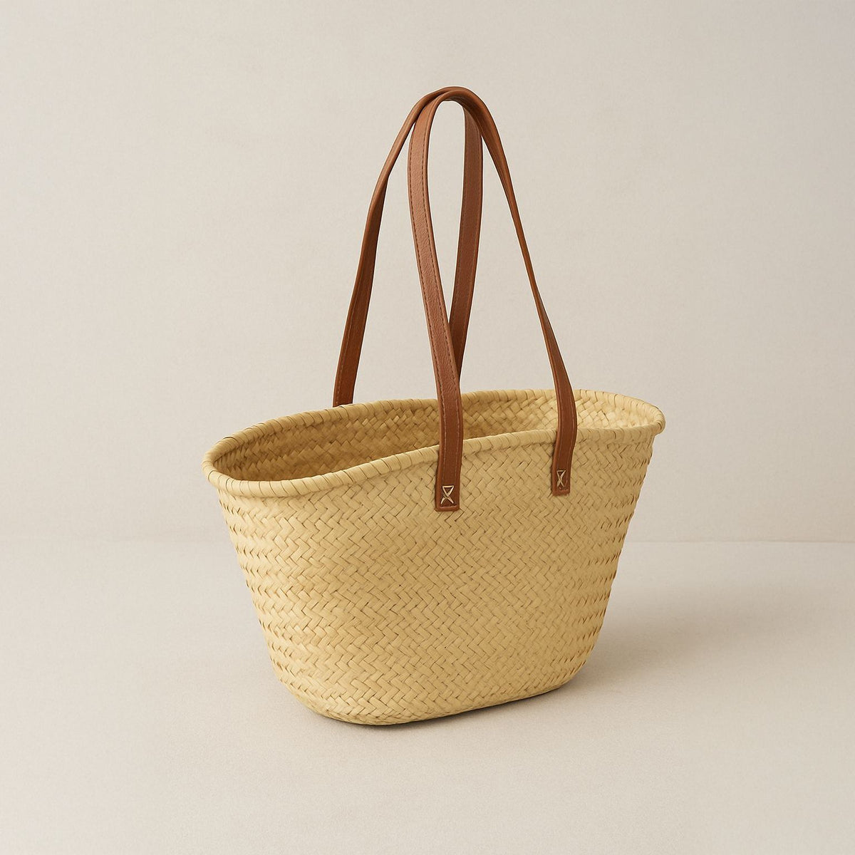 Rieten shopper met lange leren hengsels, vooraanzicht op een lichte achtergrond