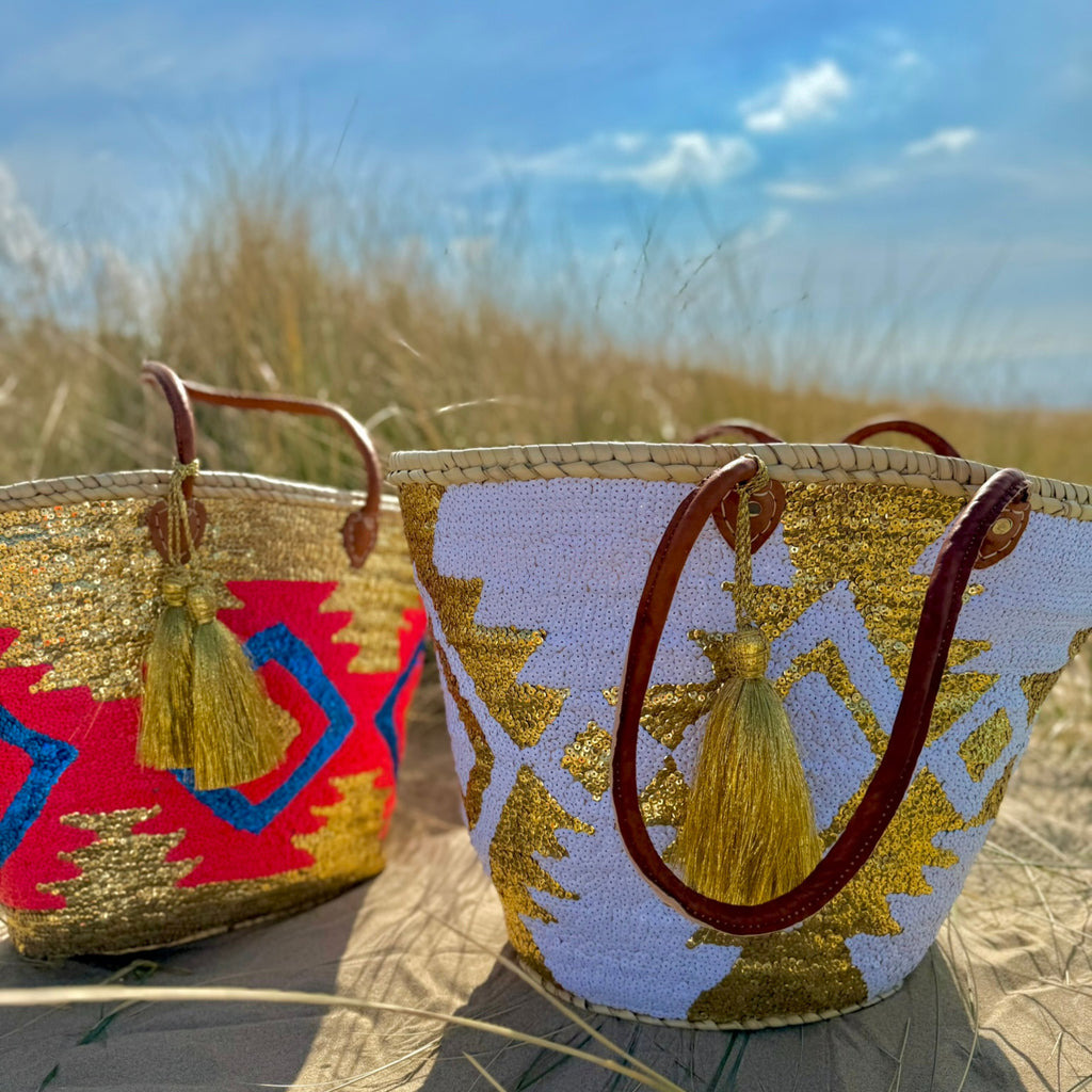 Boho rattan beach bag Aztec white and gold, next to another Aztec beach bag in the dunes