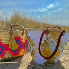 Boho rattan beach bag Aztec white and gold, next to another Aztec beach bag in the dunes