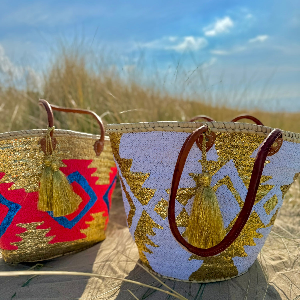 Boho rattan beach bag Aztec white and gold, next to another Aztec beach bag in the dunes