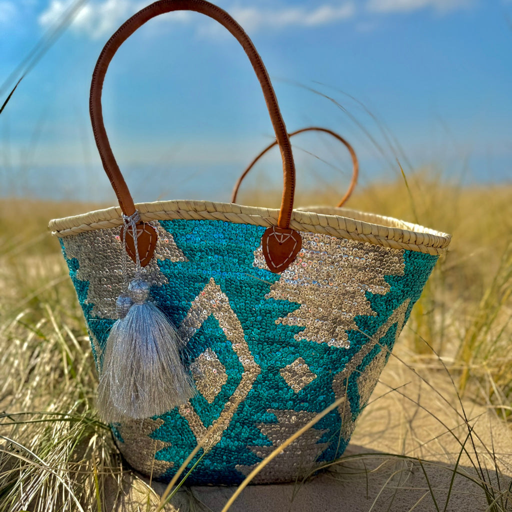 Boho rieten strandtas Aztec zilver en blauw, vooraanzicht met zilveren tassel in de duinen
