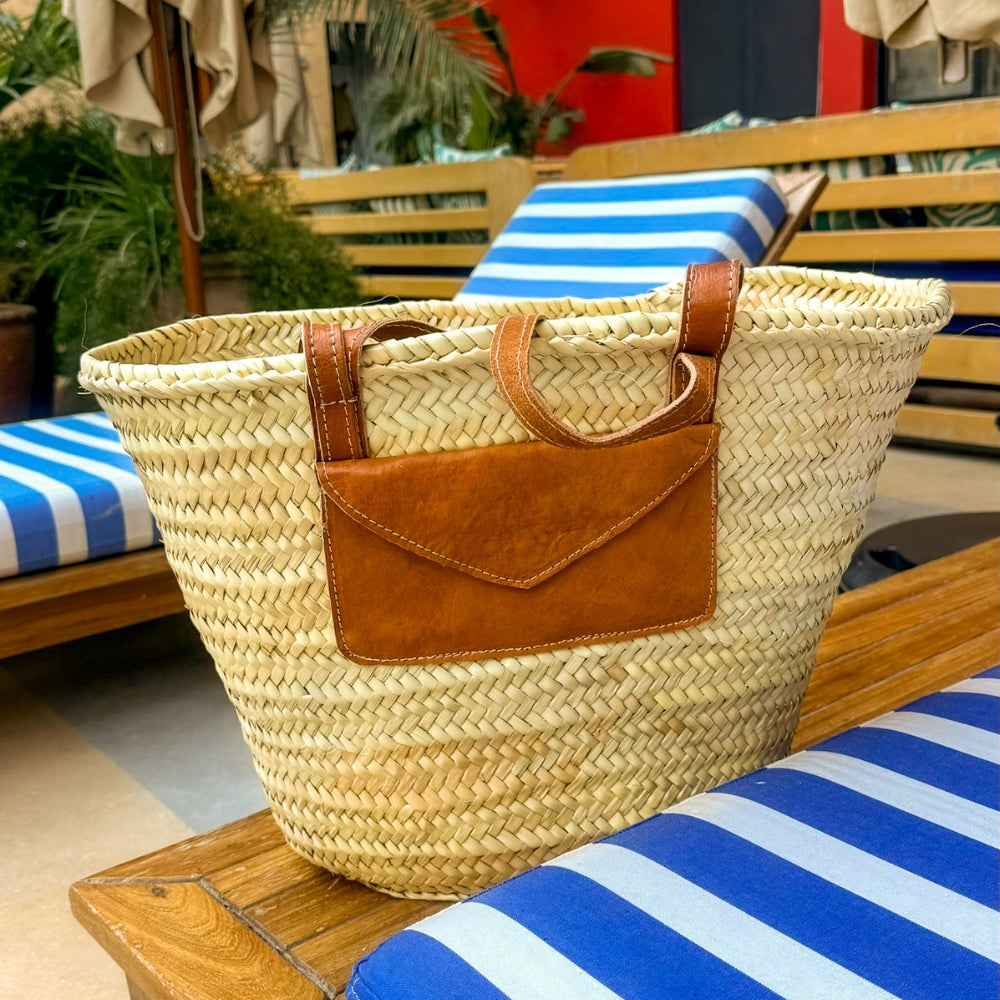 Rattan shoulder bag with leather handles and envelope pocket, with leather envelope pocket on a striped sun lounger