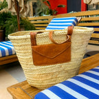 Rattan shoulder bag with leather handles and envelope pocket, with leather envelope pocket on a striped sun lounger